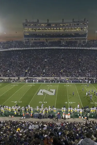 A large college football stadium at night before a game, stands full of spectators
